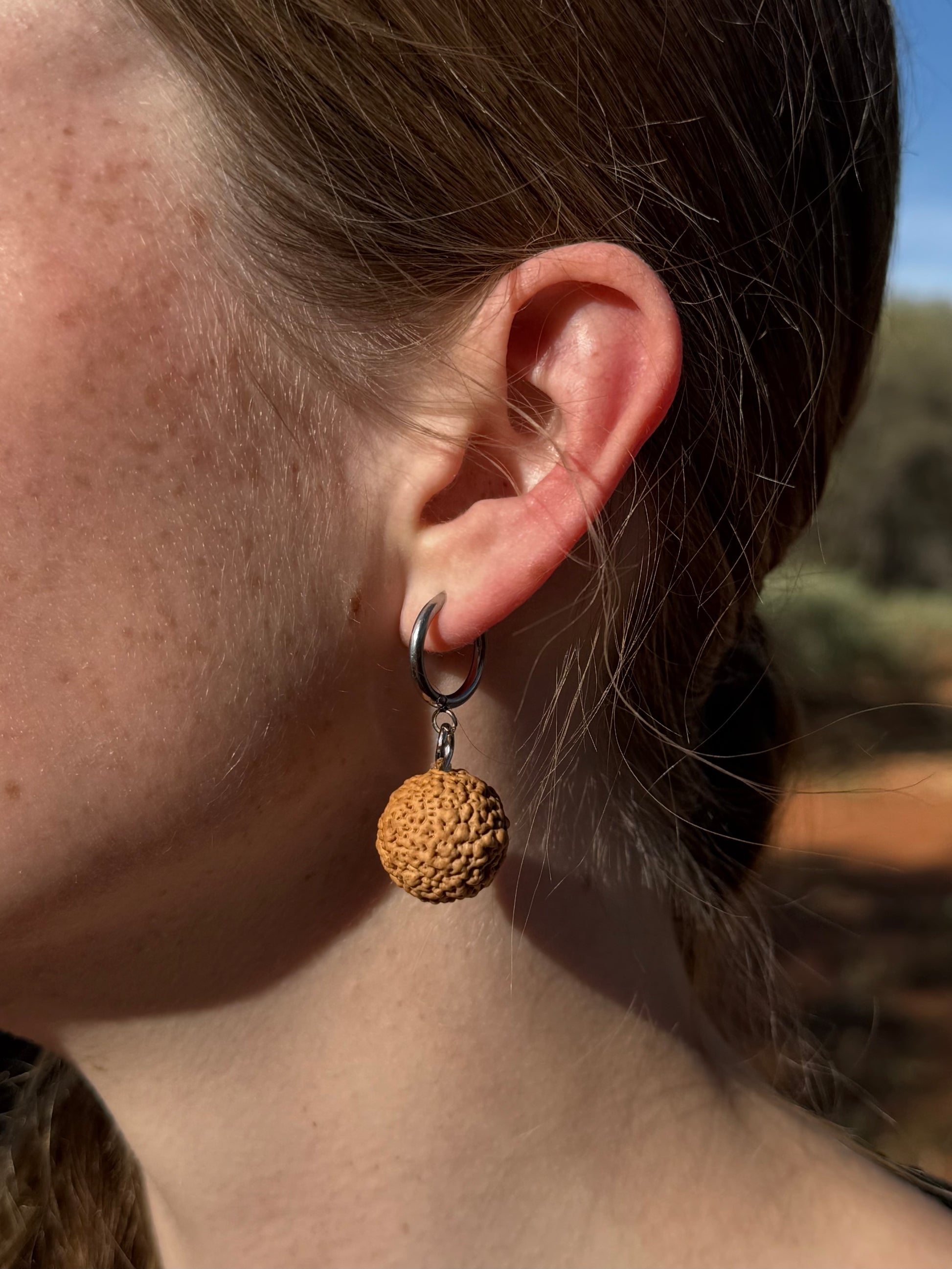 Close-up of an ear wearing a textured gold earring with a blurred natural background