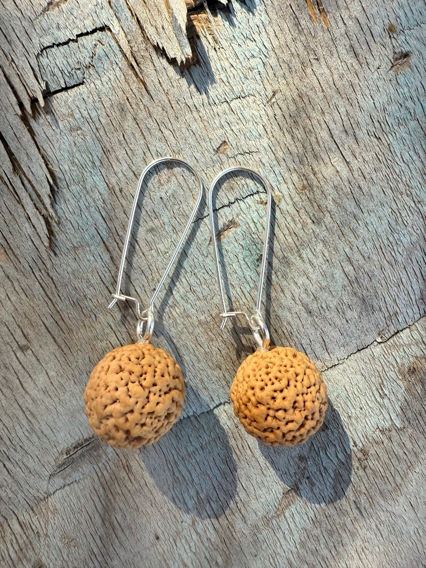 Pair of earrings with cork-like spherical pendants on a wooden surface