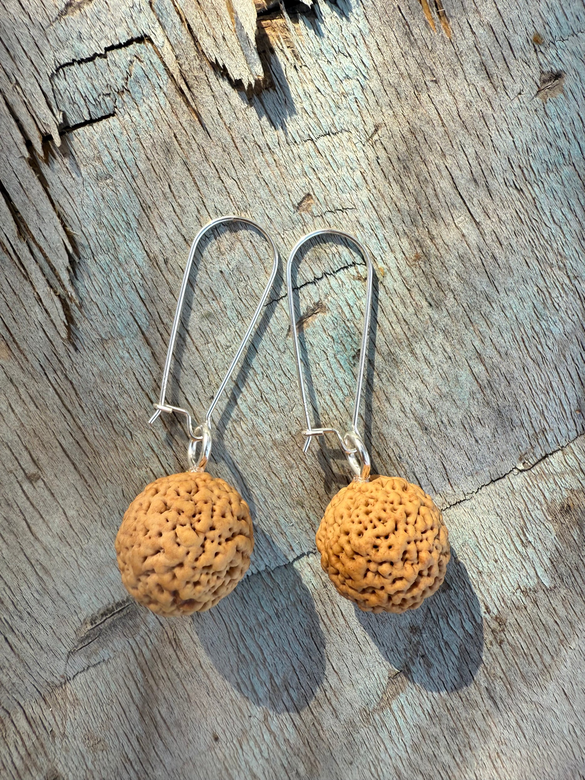 Pair of earrings with cork-like spherical pendants on a wooden surface